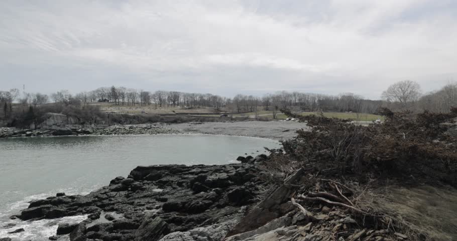 Pan across the beautiful rocky sea side view of the Portland Maine revealing the Head Light light house during a beautiful spring day with waves rolling into the rocky shore in 4k.