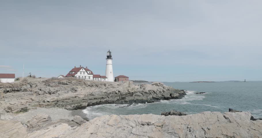 Beautiful rocky sea side view of the Portland Maine Head Light light house during a beautiful spring day with waves rolling into the rocky shore in 4k.
