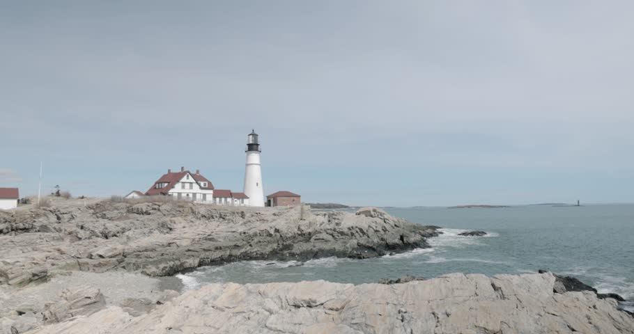 Beautiful rocky sea side view of the Portland Maine Head Light light house during a beautiful spring day with waves rolling into the rocky shore in 4k.