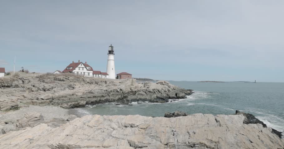 Beautiful rocky sea side view of the Portland Maine Head Light light house during a beautiful spring day with waves rolling into the rocky shore in 4k.