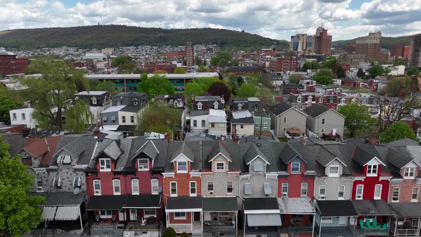 Aerial view of a colorful row of townhouses with distinct roofs, in a dense urban setting backed by a hilly landscape. Truck shot on bright spring day in American city.