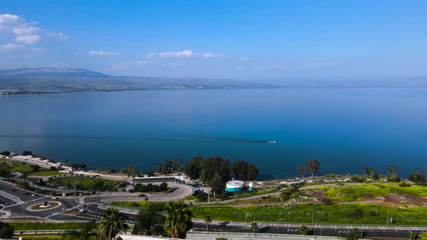 Sea of Galilee, drone shot
boat sailed on the quiet lake.
A bright spring day, blue water.
A road near the water, the Golan mountains are visible on the horizon