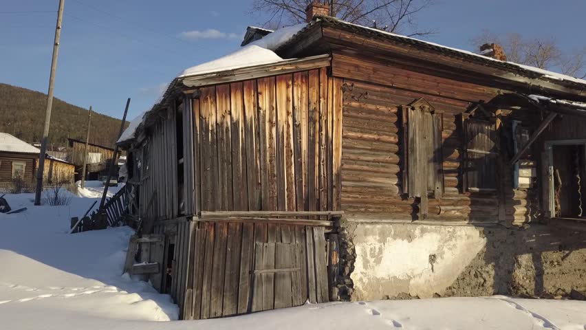 Wooden house stands in snowy field, surrounded by white landscape
