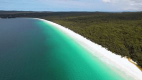 4K drone video flying backwards to reveal more of the stunning Hyams Beach, a long stretch of white sand with rainforest on one side and blue ocean waters on the other. Jervis Bay, New South Wales.