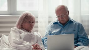 Cheerful senior couple booking a vacation on a laptop while lying in bed, engaged in shopping - Powered by Shutterstock - Get 15% off with code: PIKWIZARD15