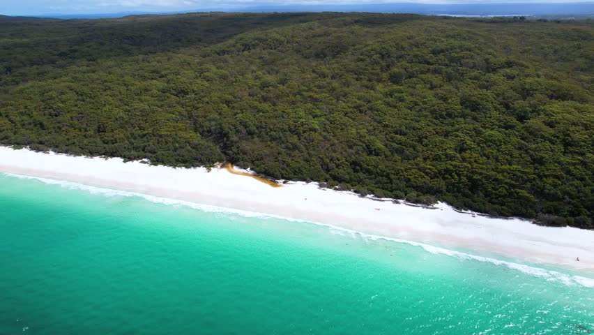 4K drone video flying backwards to reveal more of the stunning scenery surrounding Hyams Beach in Jervis Bay, a stunning white sand beach surrounded by rainforest and blue ocean water. Australia.