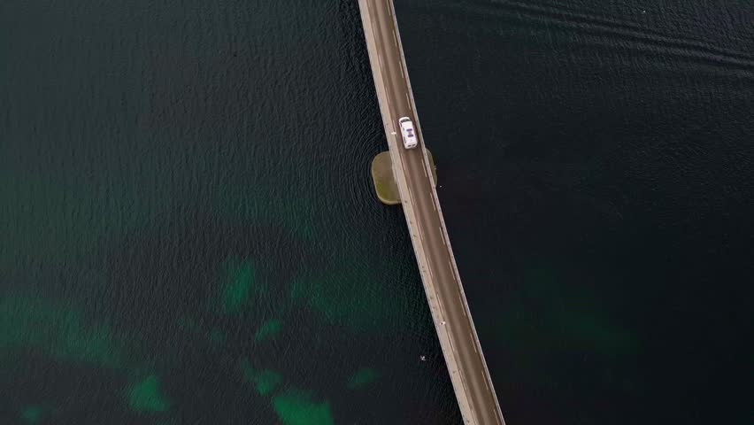 Top down view of vehicle drove across tiny bridge above the calm turqoise water in Reine Village, Norway