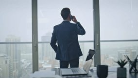 Business manager speaking cellphone looking at panoramic window luxury office back view. Confident businessman talking phone solving work tasks remotely. Handsome entrepreneur ending smartphone call - Powered by Shutterstock - Get 15% off with code: PIKWIZARD15