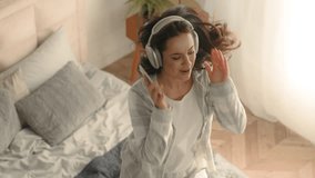 Energetic woman jumping on bed bedroom dancing hold mobile phone smartphone cellphone home headphones listen music technology active female girl enjoy sing song pastime weekend positive delight tenant - Powered by Shutterstock - Get 15% off with code: PIKWIZARD15