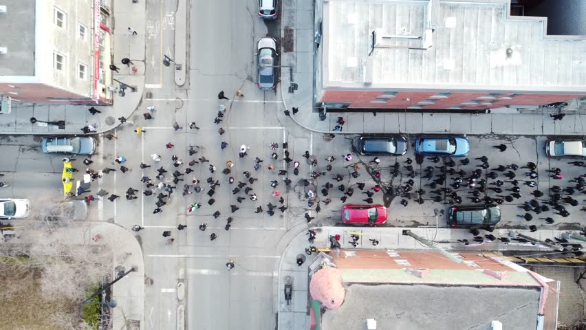 Large crowd gathers for a peaceful protest in downtown Montréal, highlighting banners and flags, on a sunny day, wide shot