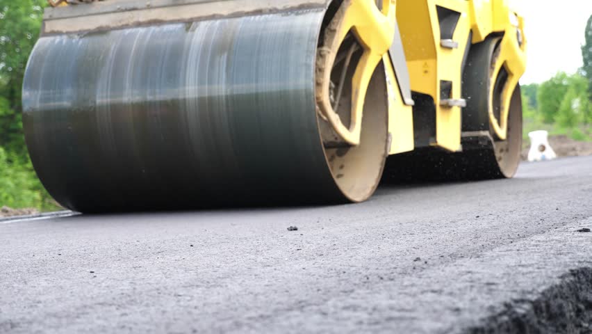 Compactor constructing highway. Steamroller slowly ride. Roadway repair by heavy machinery. Roller laying new asphalt layer. Special machinery making road. Concept of roadwork and motorway maintenance