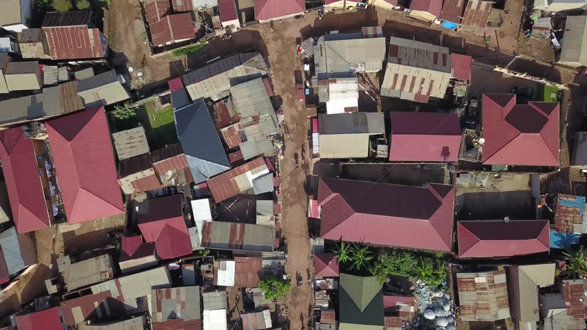 Aerial top down to cyclist on street and metal roof homes in Bukasa, Kampala city, Uganda