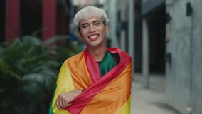 Smiling Transgender Person with Pride Flag Wrapped Around Shoulders Posing Outside to the Camera. LGBTQ Pride and Community. - Powered by Shutterstock - Get 15% off with code: PIKWIZARD15