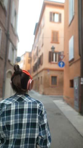 A pretty young lady, with earphones in and a smartphone in hand, hurries along the streets of a European city.