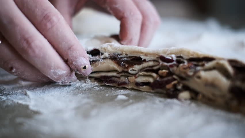 Hands delicately shaping a craffin from dough filled with chocolate, nuts, and cranberries, capturing the artistry and skill involved in making this delectable layered pastry.