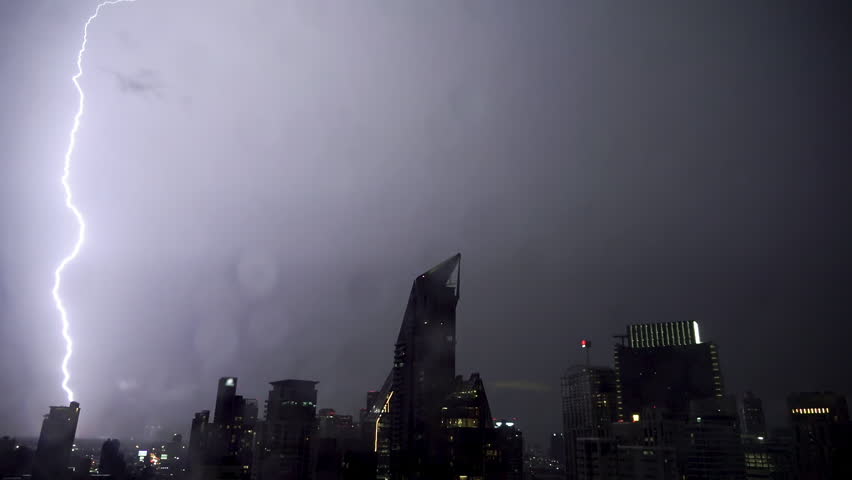Lightning and rain in modern city center of Bangkok. Storm clouds with lightning strike bolts passing over night city of Bangkok cityscape.