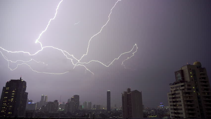 Lightning and rain in modern city center of Bangkok. Storm clouds with lightning strike bolts passing over night city of Bangkok cityscape.