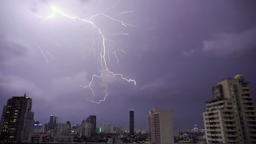 Lightning and rain in modern city center of Bangkok. Storm clouds with lightning strike bolts passing over night city of Bangkok cityscape.
