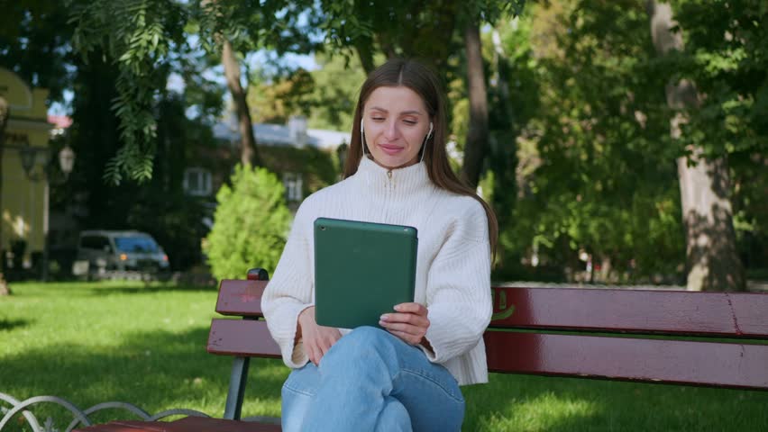 Beautiful woman with earphones having video chat via tablet in park