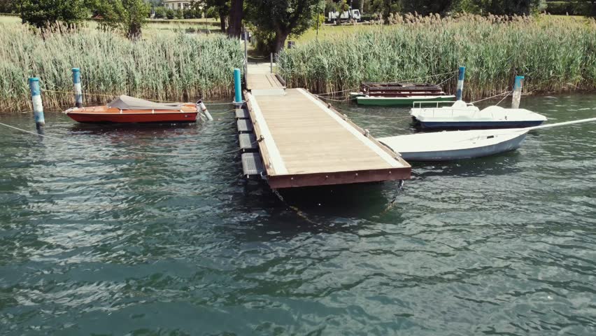 Drone shot from a small lake dock with boats to a mountain view, Italy