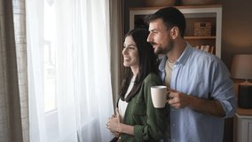 Young happy couple standing near window in their new home looking out, talking about neighbors, enjoying new life in quiet community. Man and woman enjoying new life at their new house. - Powered by Shutterstock - Get 15% off with code: PIKWIZARD15