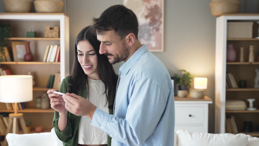 Young happy couple hugging and kissing after they realize that they will have a baby. Pregnant woman hugging her man holding positive pregnancy test stick in her hand. - Powered by Shutterstock - Get 15% off with code: PIKWIZARD15
