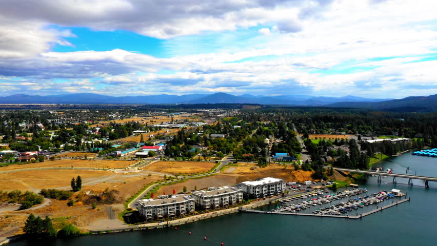 Aerial Beautiful Shot Of Harbor And Bridge In Town, Drone Flying Backwards Over Rippled River Under Cloudy Sky - Coeur d