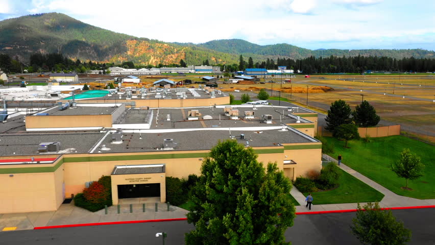 Aerial: Drone Panning Descending Shot Of People Walking Outside Sheriff Office By Mountains - Coeur d'Alene, Idaho