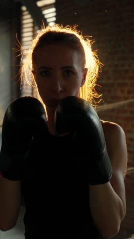 Confident aggressive woman boxer punching to camera, vertical frontal portrait in gym. Athletic lady training in fight club, do sport in fitness center, release aggression and psychological problems