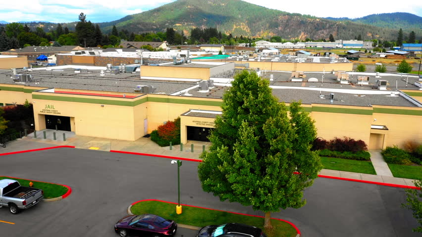 Aerial: Drone Forward Tilt Down Shot Of Sheriff Office By Mountains In City Against Cloudy Sky - Coeur d'Alene, Idaho