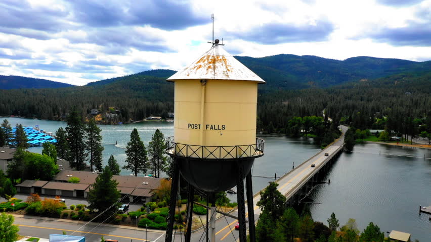 Aerial Panning Shot Of Tall Water Tower By Rippled River In Town - Coeur d