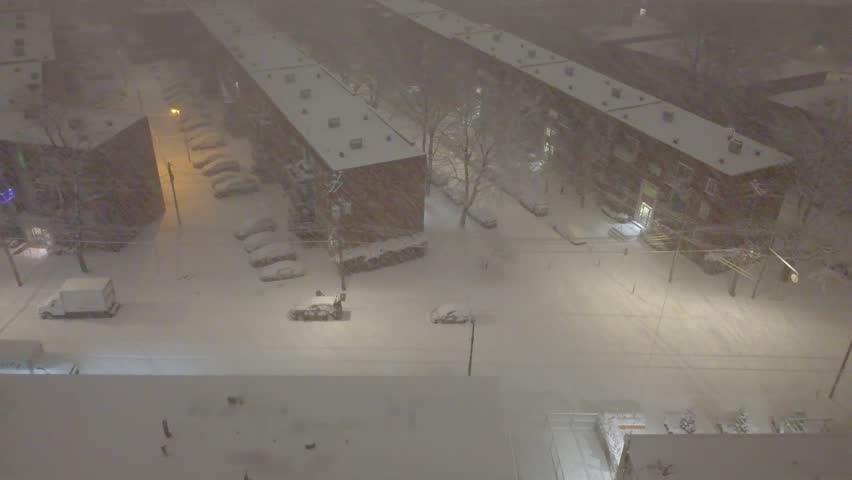 Winter night in Montreal with snowfall covering streets and parked cars, cityscape