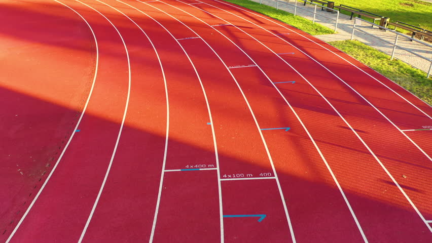 Drone follows eight lane track start line with light across red empty rubber