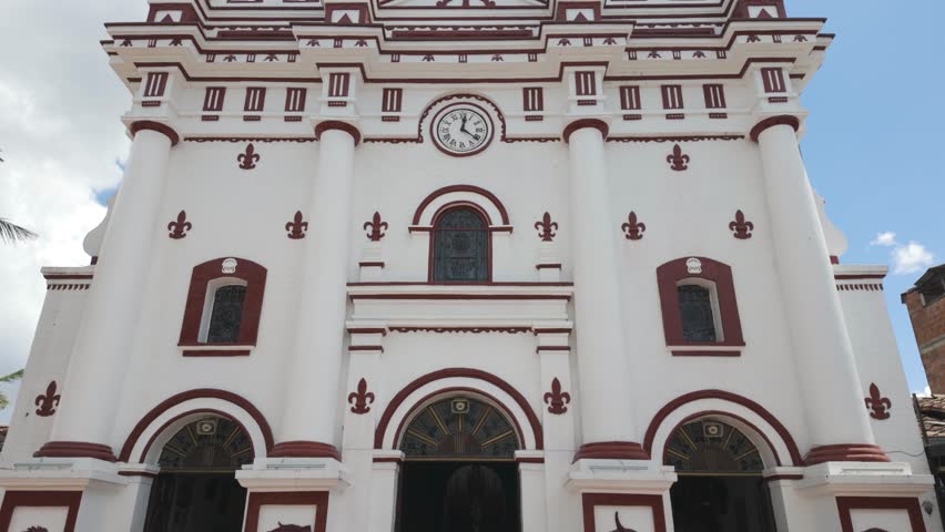 White and red church with a clock tower under a blue sky in Guatapé, Colombia