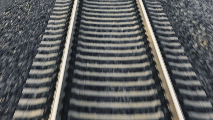 Railway line installed on gravel ground at rural site closeup. Motion along railroad during journey view from train cabin. Transport system