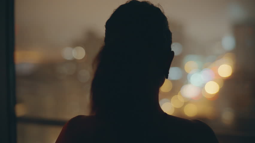 Night model looking panoramic window at dark flat back view. Silhouette woman thinking future planning in contemporary luxury house. Brunette lady contemplating evening lights cityscape dreaming alone