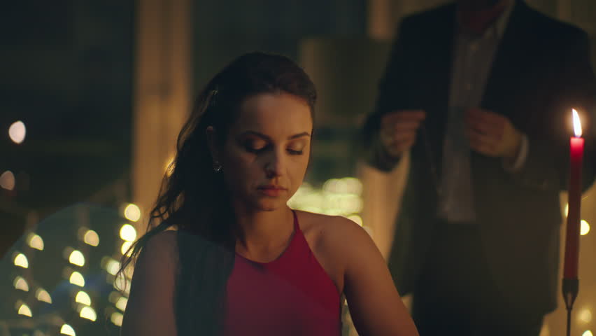 Boyfriend wearing necklace girlfriend neck making surprise at romantic dinner closeup. Happy surprised woman reacting at gift feeling happy at night lights background. Positive couple celebrating date