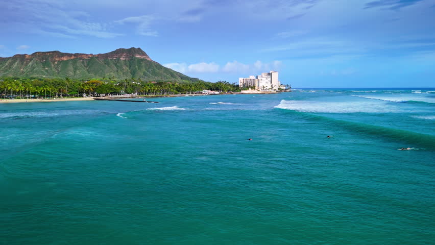 Low aerial shot tracking over breaking waves and surfers, Waikiki Beach, Honolulu, Hawaii