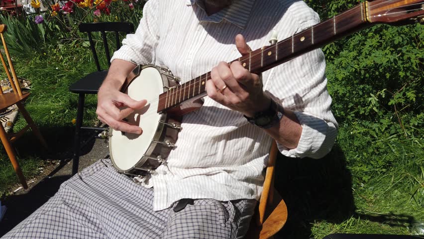 A musician plays the banjo accompanied by a violinist during a sunny day.
