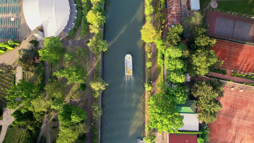 Aerial drone view of Bega river in Timisoara, Romania. View of the river with floating boat, greenery and buildings on the both sides of the river
