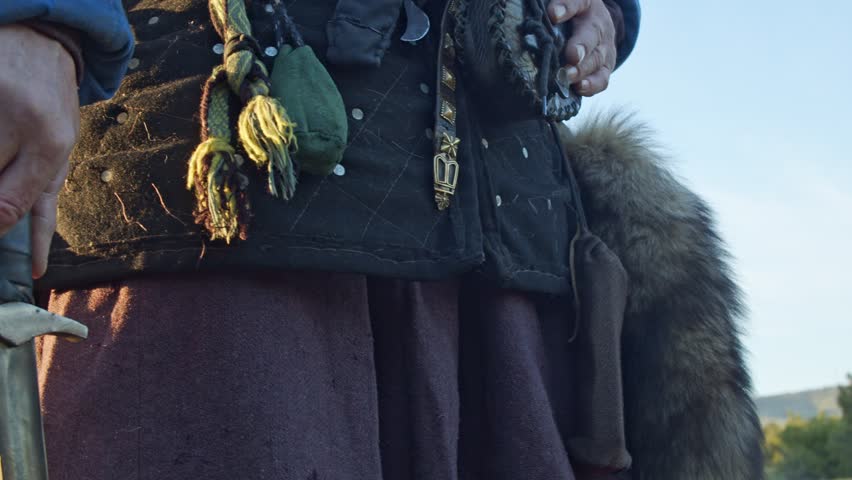 The hand of a man in a medieval knight costume holds a sword in the bright rays of the sunset. Close-up. Historical reconstruction.