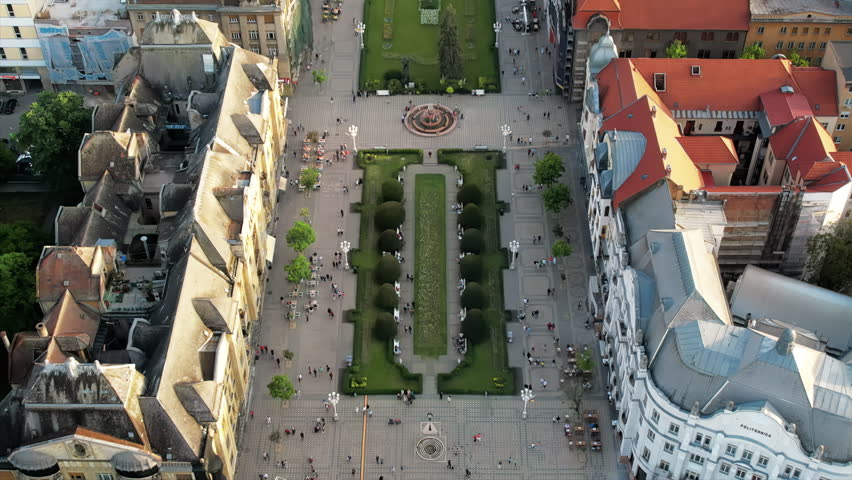 Aerial drone view of Timisoara at sunset, Romania. View of the Victory Square with multiple walking people and historical buildings around, Orthodox Cathedral