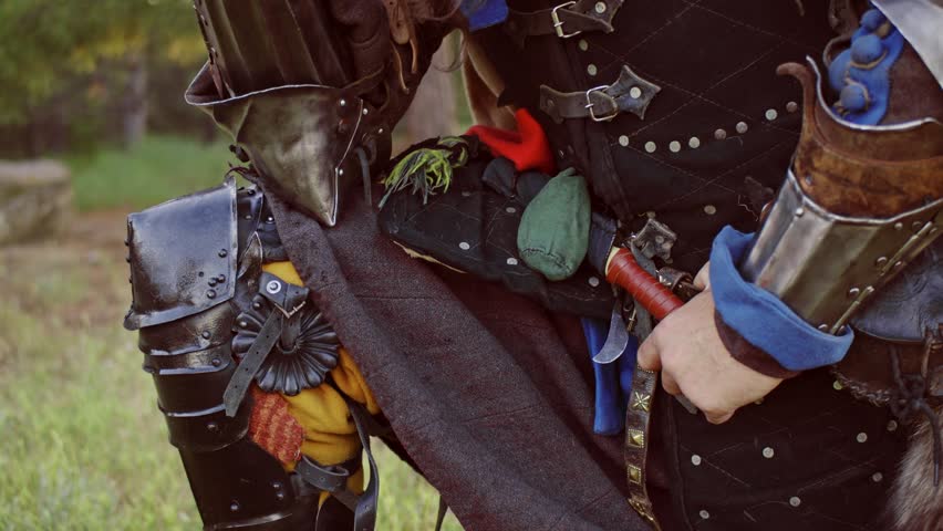 A man in a medieval knight costume. Close-up of hands with a sword in front of the face against the backdrop of nature