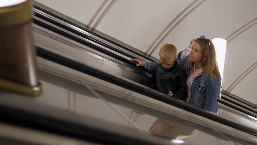 A caring mother and son climb the escalator in the subway and have a fun conversation, mom hugs her son. The movement of the escalator underground.