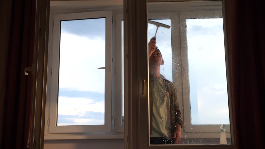 a man in headphones listens to music and washes a window in his apartment