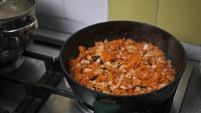 Chopped onions and grated carrots sizzle in a pan, their colors intensifying as they cook. A spatula stirs the mixture, ensuring even browning and releasing a delicious aroma.