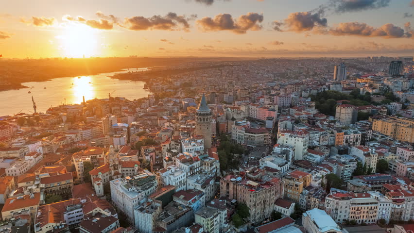 Aerial drone hyperlapse view of Istanbul at sunset, Turkey. Multiple residential buildings around the Galata tower, nightlights, Golden Horn waterway on the background
