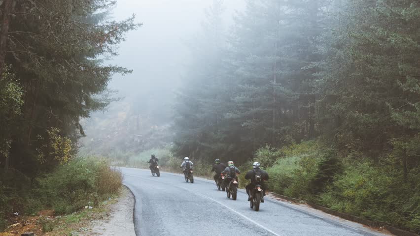 A group of men ride a motorcycle along a road in the mountains in the fog
