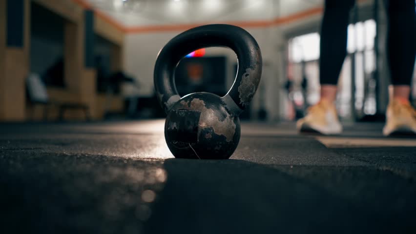 close-up In the gym a girl trainer lifts a standing black weight from the floor