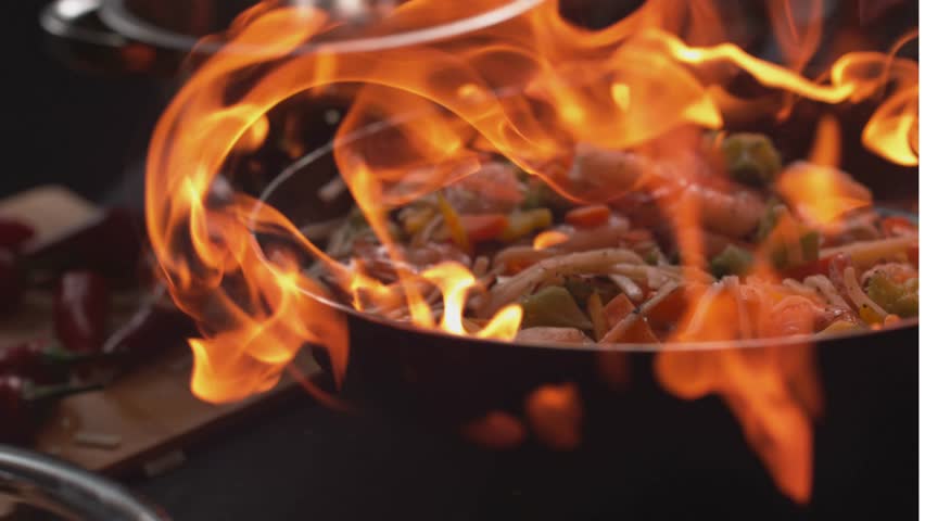 Super Slow Motion Shot of Wok Pan with Flying Ingredients in the Air and Fire Flames. 